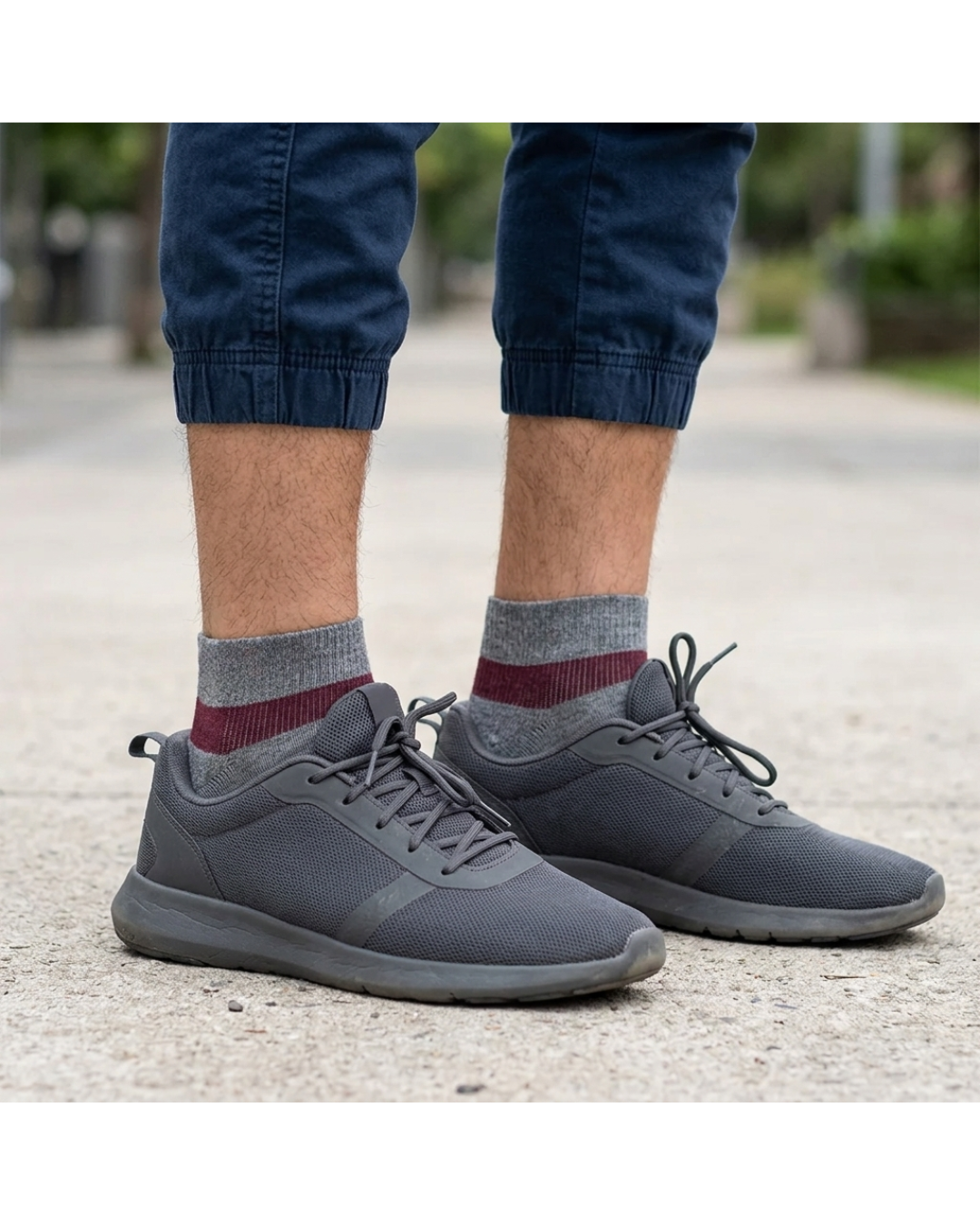 Man wearing grey marl and burgundy ankle compression socks and grey sneakers standing outdoors.