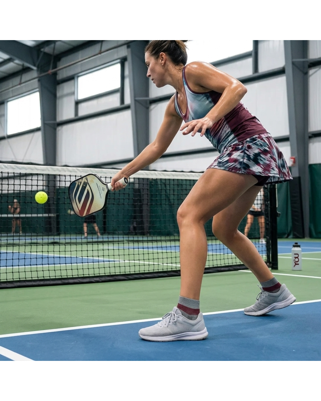 Woman wearing grey marl and burgundy ankle compression socks while playing pickleball on an indoor court.