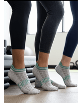 Three people standing side-by-side in a gym, wearing gray and green athletic low-cut compression ankle socks paired with dark leggings.